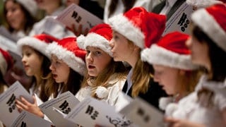 Kinder mit Weihnachtsmann-Mützen singen Weihnachtslieder. Ob in der Kirche, im festlich geschmückten Wohnzimmer oder auf dem Weihnachtsmarkt: Alle Jahre wieder erklingen Weihnachtslieder. 