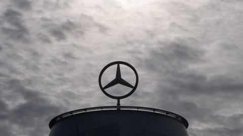 Ein Mercedes-Stern steht auf einem Gebäude unter wolkenverhangenem Himmel.