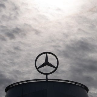 Ein Mercedes-Stern steht auf einem Gebäude unter wolkenverhangenem Himmel.