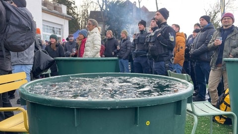 Zahlreiche Menschen stehen neben Tonnen mit Eiswasser, darunter auch Polizisten. 