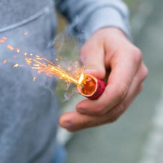 Ein Mann hält einen brennenden Böller in der Hand. (Symbolbild) Polizei und Ärzte fordern ein Böller-Verbot.