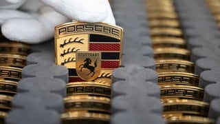 Ein Mitarbeiter der Porsche AG zeigt im Stammwerk in Zuffenhausen Porsche-Wappen, die auf Motorhauben des vollelektrischen Porsche Taycan, angebracht werden.