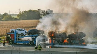 Einsatzkräfte der Feuerwehr löschen in Brand geratene Autos auf einem Transporter. 