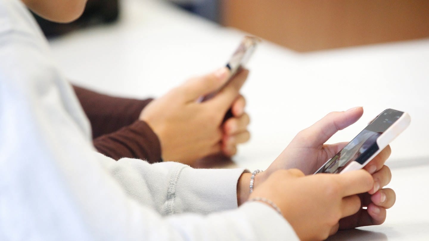 Ein Schüler sitzt an einem Tisch mit einem Smartphone in der Hand.
