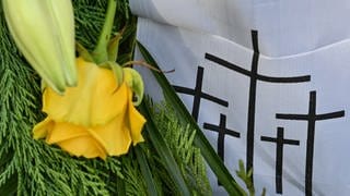 Eine gelbe Rose und schwarze Kreuze auf weißem Stoff: Symbolbild zum Volkstrauertag