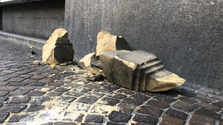 Mehrere Trümmerteile aus beigem Sandstein liegen auf dem Bürgersteig.