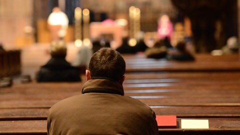 Mann sitzt in einer hölzernem Bank in einer Kirche.