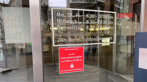 Am Eingang zur Hauptgeschäftstelle der Sparkasse Lörrach-Rheinfelden in Lörrach hängt ein rotes Hinweisschild. Darauf steht: "Ab sofort: Foyernutzung täglich von 5 bis 23 Uhr."