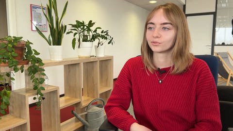 Frau mit braunen Haaren sitzt an einem Schreibtisch. 