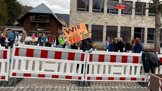 Schönauer Schüler demosntrieren gegen Bauzaun. Auf einem Schild steht: Wir haben weniger Platz als Tiere im Zoo. Das Mädchen, das das Schild hält, steht hinter dem rot-weißen Bauzaun.