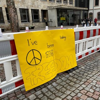 Auf einem gelben Plakat steht in Schwarz: I've been looking for a freedom. Das Plakat hängt an dem rot-weißen Bauzaun, der den Schönauer Schulhof verkleinert.
