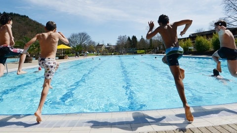 Vier Kinder springen vom Beckenrand ins Wasser.