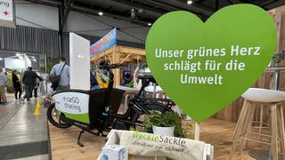 Ein großes grüner Herz aus Pappe steht auf der greenflair Messe für Nachhaltigkeit in Freiburg. Darunter nachhaltige Beutel und Produkte. 