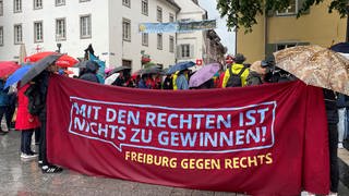 Menschen mit Regenschirmen hinter einem Plakat mit der Aufschrift "Mit den Rechten ist nichts zu gewinnen! Freiburg gegen Rechts".