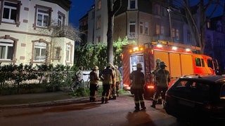 Einsatzkräfte der Feuerwehr stehen an einem Wohnhaus, in dessen Untergeschoss sich eine Explosion ereignete.