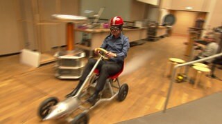 Ausgestattet mit Helm und Motorradbrille - so fährt Professor Fischer auf seinem Raketen-Go-Kart mit CO2-Antrieb durch den Hörsaal. 