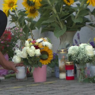 Kerzen und Blumen stehen auf dem Boden. Auf einer Tafel steht "Fly".