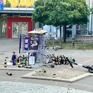 Zwei Einkaufswagen liegen umgekippt auf dem Lederleplatz, umgeben von leeren Flaschen und Müll.