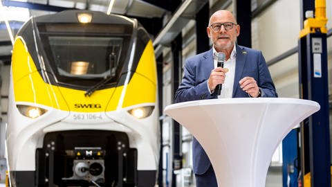 Baden-Württembergs Verkehrsminister Winfried Hermann (Grüne) steht in einer Werkshalle vor einem Zug mit dem Logo der SWEG. Im Ortenaukreis sollen Ende des Jahres batteriebetriebene Regionalzüge fahren - als Beitrag zum Klimaschutz.