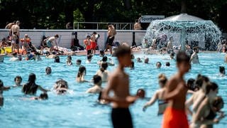 Ein Schwimmbecken in einem Freibad mit vielen Menschen im Sommer. 