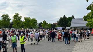 Viele Menschen haben sich vor einer kleinen Bühne versammelt, einige tragen gelbe Westen.