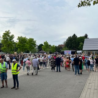 Viele Menschen haben sich vor einer kleinen Bühne versammelt, einige tragen gelbe Westen.