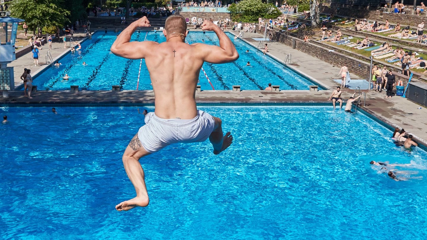 Ein Mann springt ins das Schwimmbecken eines Freibads. Er ist von hinten zu sehen.