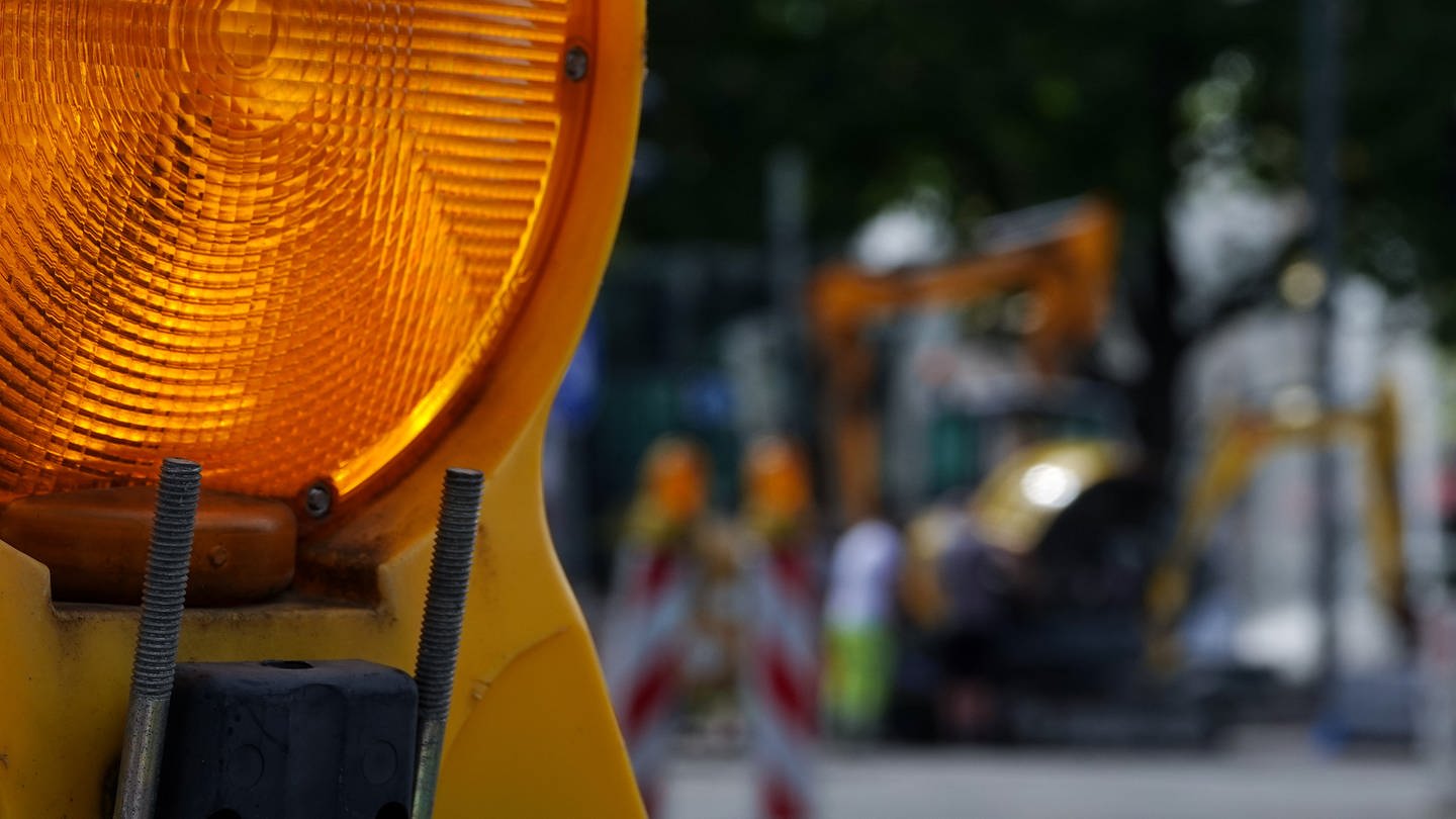 Eine Baustellenlampe im Vordergrund, im Hintergrund unscharf ein Bagger