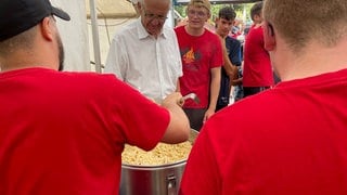 Kretschmann schaut in einen riesigen Topf mit Spätzle