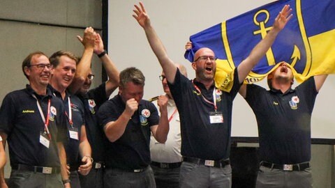 Das Siegerteam des Bundeswettbewerbs des DRK kommt aus Ibbenbüren. Männer in schwarzen T-Shirts strecken jubelnd ihre Arme in die Luft.