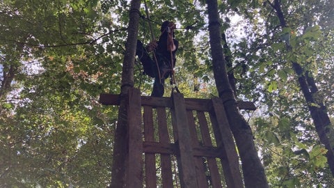 Ein vermummter Aktivist hängt im Dietenbachwald in Freiburg in Klettermontour in einem selbstgebauten Baumhaus.