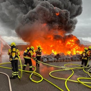 Feuerwehrleute löschen mit gelben Schläuchen den Brand auf einem großen Hof.