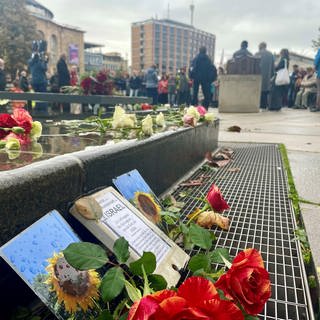 Menschen haben sich auf dem Platz der Alten Synagoge in Freiburg versammelt, am Brunnen liegen Blumen.