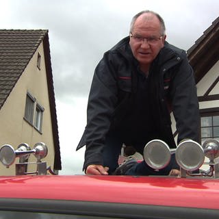 ein Mann kniet auf einem Dach eines Feuerwehrautos, davor sind Martinshörner zu sehen