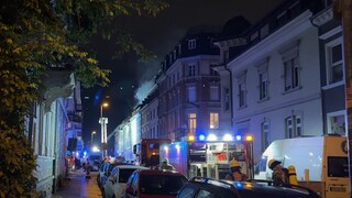 Ein Haus ist zu sehen. Oben raucht es. Auf der Straße davor stehen Einsatzwägen mit Blaulicht.