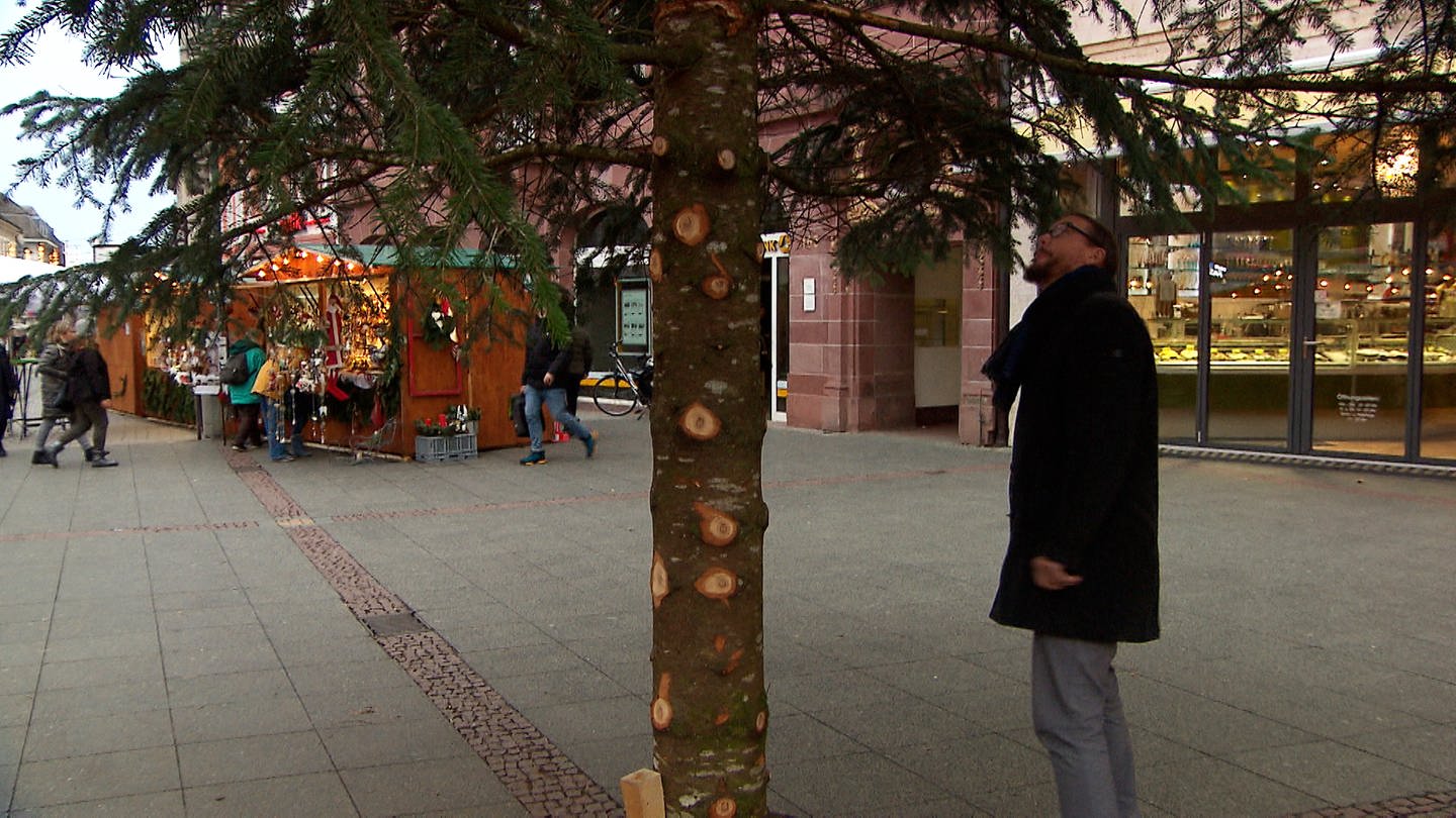 Ein Mann steht neben dem Weihnachtsbaum, dem die Äste abgeschnitten wurden.