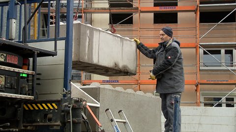 Ein Bauarbeiter befördert mit einem Baukran Material von einem Lastwagen.
