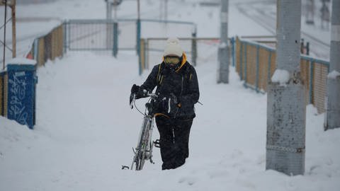 Eine Frau schiebt ihr Fahrrad durch den Schnee.