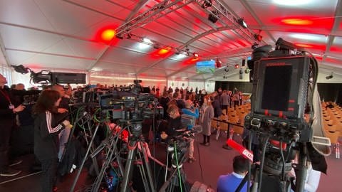 Journalisten mit Mikrofonen und Kameras in einem Festzelt.