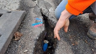 Eine Hand zeigt auf tiefe Risse in einer Straße.