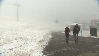 Wanderer laufen auf dem Feldberg durch Niebel und Schneerieseln.