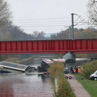 Ein Zug in einem Kanal, zerbrochen, Rettungswagen stehen vor den Brückenpfeilern