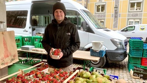 Obstbauer David Sexauer auf dem Freiburger Münstermarkt mit einer Schale Erdbeeren in der Hand