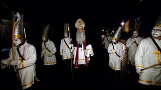 Die Dietinger Klausen ziehen durch die Straßen. Mit weißen Gesichtern, weißen Gewändern und Kronen auf dem Kopf. Bei ihnen ist ein Bischof mit Mitra und das Nussaweible im Umhang.