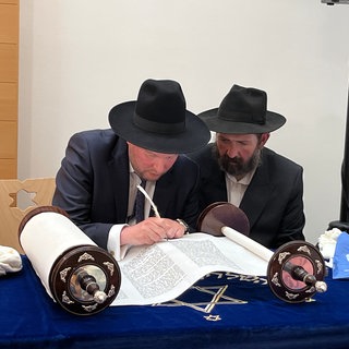 Die Torarolle liegt auf einem Tisch in der Rottweiler Synagoge während Landesrabbiner Moshe Flomenmann mit Unterstützung von Sofer Boruch Lamdan die letzten 12 Buchstaben mit einer Feder auf das Pergament geschrieben werden. 