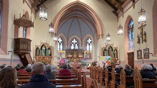 Auf diesem Bild ist die Heilige-Geist-Kirche in Laufenburg zu sehen. Sie wird von Kerzen beleuchtet. Vorne steht ein Priester und auf den Bänken sitzen die Gläubigen.