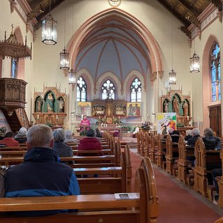 Auf diesem Bild ist die Heilige-Geist-Kirche in Laufenburg zu sehen. Sie wird von Kerzen beleuchtet. Vorne steht ein Priester und auf den Bänken sitzen die Gläubigen.