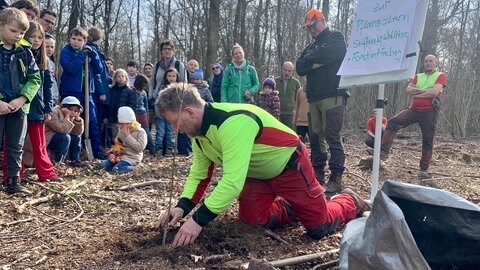 Mann pflanzt Baum vor Gruppe ein 