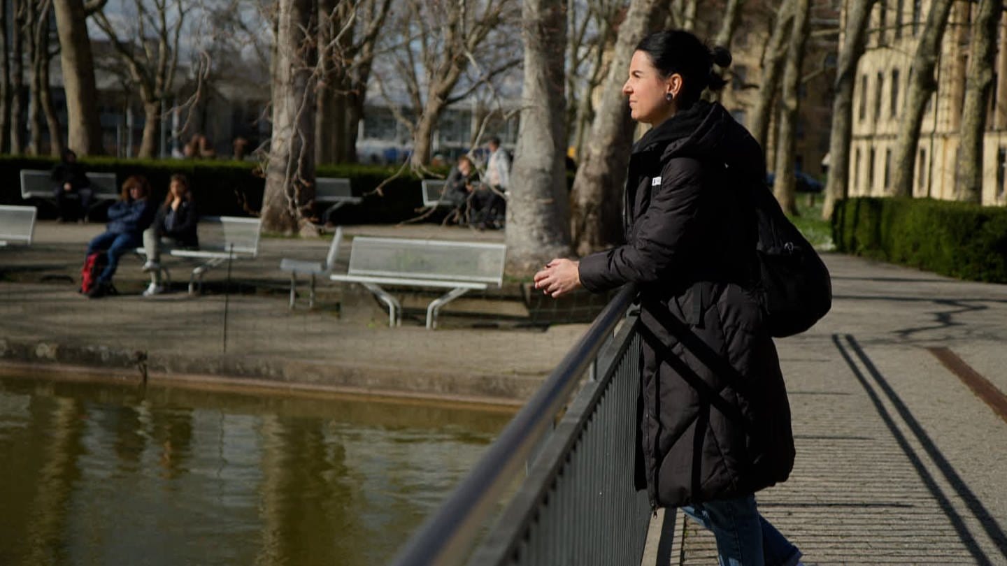 Sina Frehner steht auf einer Brücke auf dem Gelände der Uniklinik Freiburg und schaut nachdenklich in den Teich vor ihr.