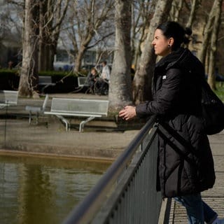 Sina Frehner steht auf einer Brücke auf dem Gelände der Uniklinik Freiburg und schaut nachdenklich in den Teich vor ihr. 